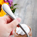A hand holding a Master's Gauge by World Tableware stainless steel dessert spoon over a cup of whipped cream.