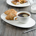 A white porcelain cup of coffee on a saucer with a plate of croissants.