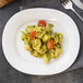 A Villeroy & Boch white porcelain oval platter with pasta, pesto, and tomatoes on a table.