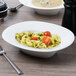 A Villeroy & Boch white porcelain oval bowl filled with pasta, tomatoes, and vegetables.