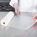 A person in a chef's uniform cutting a roll of VacPak-It full mesh vacuum packaging bags with scissors.