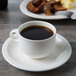 A Villeroy & Boch white porcelain stackable cup of coffee on a saucer on a table with a plate of food.
