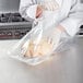 A person in a white coat wearing gloves vacuum sealing a chicken in a VacPak-It plastic bag.
