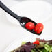 A black Cambro salad bar spoon with tomatoes on it.