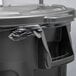 A black Rubbermaid BRUTE trash can with a lid on top and a plastic bag inside.
