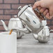 A hand pouring coffee into a Vollrath stainless steel teapot.
