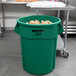 A green Rubbermaid BRUTE trash can filled with potatoes.