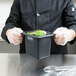A chef using a Carlisle black plastic food pan on a counter.