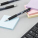 A Uni-Ball Signo 207 pen with a black barrel on a desk with post it notes.