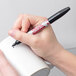 A person using a Sharpie black industrial permanent marker to draw on a white mug.