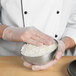 A person in white gloves holding a Matfer Bourgeat stainless steel hemisphere mold filled with rice.