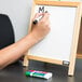A hand holding an Expo low-odor dry erase marker writing on a white board.