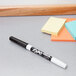 A black Expo dry erase marker on a table next to a yellow sticky note.