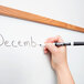 A hand using a black Expo fine point dry erase marker to write "December" on a whiteboard.