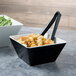 A black square melamine bowl full of croutons on a salad bar counter.