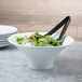 A white fluted melamine pedestal bowl filled with salad on a table with a fork.