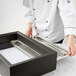 A chef in a white coat using a Vollrath black wooden display base for a metal tray.