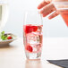 A hand reaching for a Reserve by Libbey chisel cooler glass filled with pink liquid and raspberries.