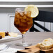 A Reserve by Libbey Prism goblet filled with ice tea, ice, and a lemon slice on a table.