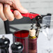 A hand with a red Pulltap's Corkscrew opening a bottle of wine.