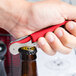 A hand using a Pulltap's Original Waiter's Corkscrew with a red handle to open a beer bottle.