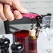A hand using a Pulltap's Original Waiter's Corkscrew with a dark pink handle to open a bottle of wine.