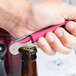A hand using a dark pink Pulltap's Original Waiter's Corkscrew to open a bottle of wine.