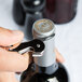 A hand using a Pulltap's Original Waiter's Corkscrew with a white handle to open a bottle of wine.