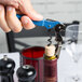 A hand with a blue Pulltap's Original Waiter's Corkscrew opening a bottle of wine.