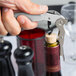 A hand using a Pullparrot waiter's corkscrew with a white handle to open a wine bottle.
