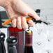 A hand holding a Pulltap's Original customizable waiter's corkscrew with an orange handle opening a bottle of wine.