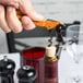 A hand using a Pulltap's Original orange corkscrew to open a bottle of wine.