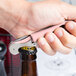 A hand using a Pulltap's Original Waiter's Corkscrew with a light pink handle to open a bottle of beer.