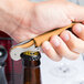 A hand opening a bottle with a Pulltap's Original Waiter's Corkscrew with a hazelnut handle.