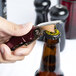 A finger with a red Franmara waiter's corkscrew opening a bottle of beer.