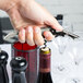 A hand holding a Pulltap's Original silver gray corkscrew opening a wine bottle.