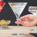 A close-up of a hand holding a Libbey Crosshatch Martini Glass with liquid and a strawberry.