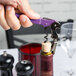 A hand using a Pulltap's Original Waiter's Corkscrew with a purple handle to open a bottle of wine.