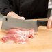 A person using a 10" stainless steel meat cleaver to cut meat on a cutting board.