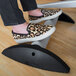 A person's feet wearing leopard print shoes on a Safco black aluminum footrest.