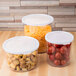 A wooden table with three Cambro plastic crocks filled with food. One crock contains tomatoes, another contains cheese.