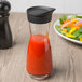 A Libbey carafe with a red liquid in it on a counter next to a salad.