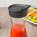 A Libbey carafe with a black rubber lid on a table with a salad.