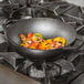 A Lodge pre-seasoned cast iron wok on a stove with vegetables cooking.