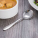 A bowl of soup with a Oneida Scroll stainless steel bouillon spoon on a table.