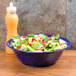 A table with a bowl of salad in a cobalt blue New Yorker catering bowl.