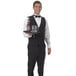 A waiter in a tuxedo holding a tray with a beer and a mug.