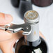 A hand using a Franmara Duo-Lever Corkscrew with a white enamel handle to open a bottle of wine.