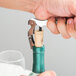 A person using a Franmara Duo-Lever corkscrew with a white enamel handle to open a bottle of wine.