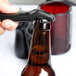 A hand using a Franmara Traveler's Black plastic bottle opener to open a beer bottle.